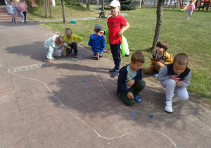grupka dzieci gra w kapselki i pstryka je po wyznaczonym torze